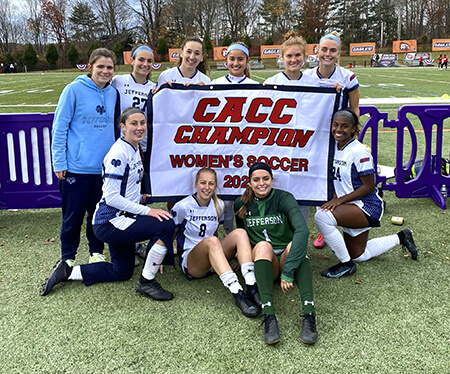 Jeena and her teammates flanking their 2022 CACC Champions banner on the soccer field.
