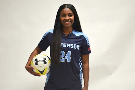 Jeena wearing her Thomas Jefferson University jersey and holding a soccer ball.