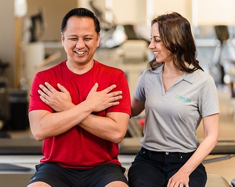 Patient and physical therapist sit on a bench and smile while working together on therapy exercises.
