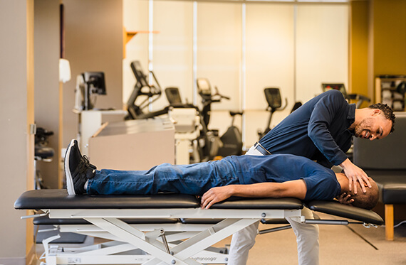 A patient laying on their back on a table while a therapist stretches their neck
