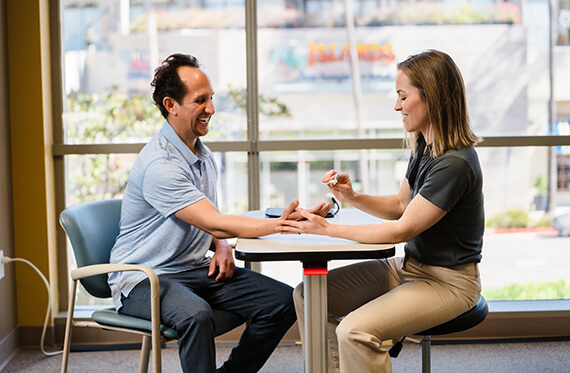 A patient and therapist sitting at a table together and smiling while the therapist performs manual therapy on the patient's hand